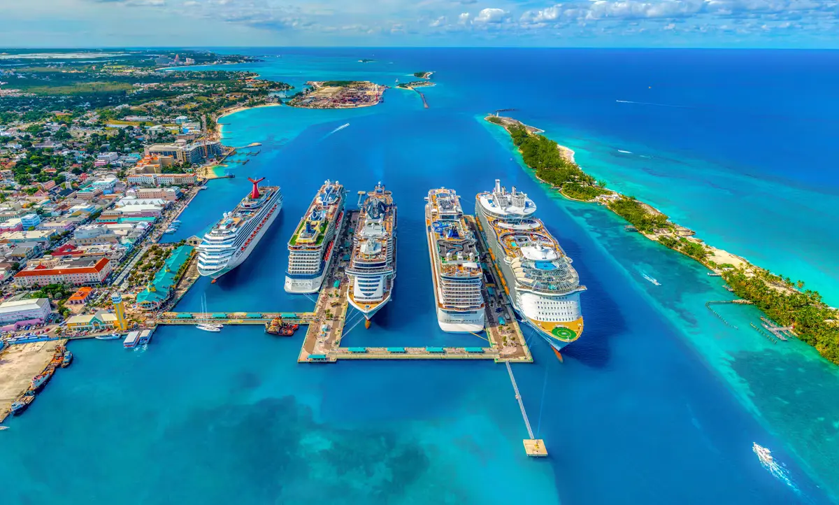 Aerial view of five cruise ships berthed side by side at Nassau's Prince George Wharf, with downtown on the left and Paradise Island's green shore across turquoise water