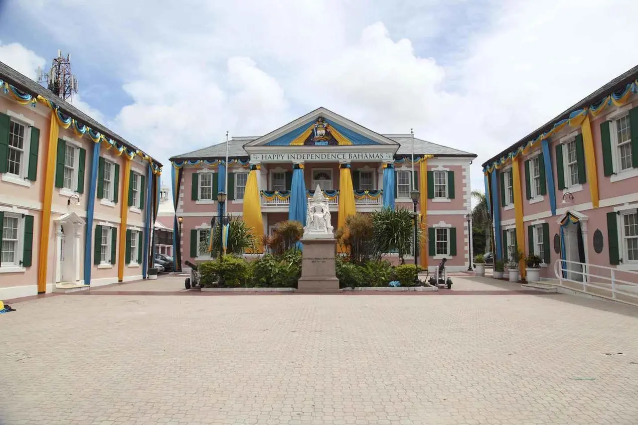 Pink colonial government buildings with blue shutters around a white statue in Parliament Square, Nassau