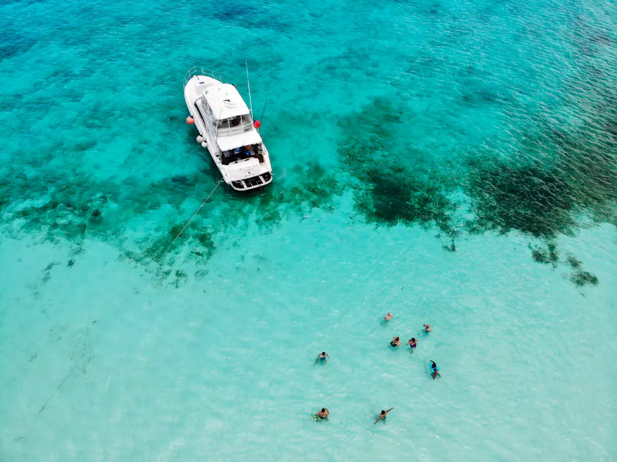 Aerial view of a white tour boat anchored in turquoise shallows at El Cielo with a group of snorkelers floating nearby