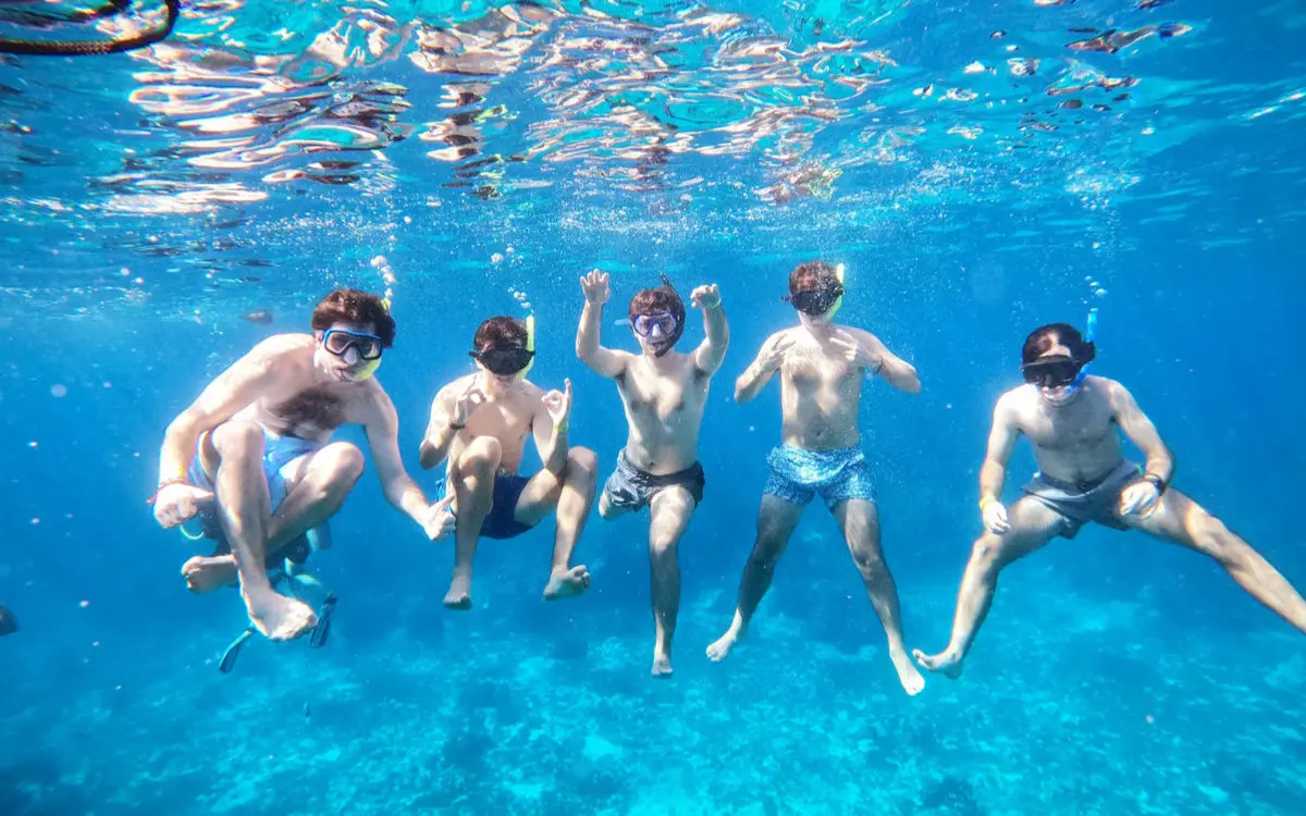 Five snorkelers in a row in clear blue water, seen from below with the sunlit surface above them