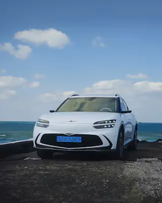 A white SUV parked on a coastal lookout with the blue sea and scattered clouds behind it